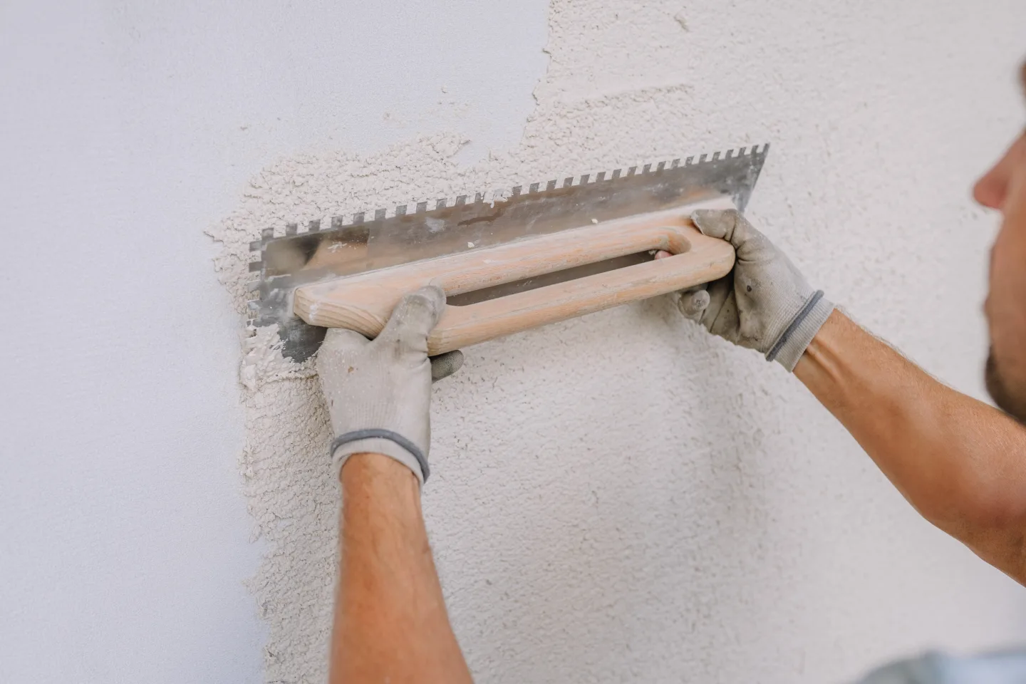 Ein Arbeiter glättet Gips an einer Wand mit einer gekerbten Kelle mit Kalkputz, wobei er sich auf eine 
